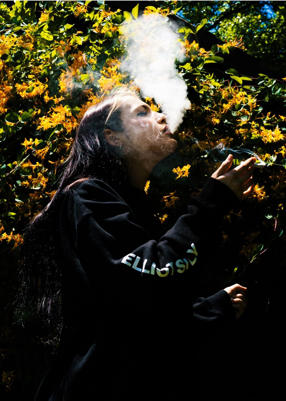 A Girl posing with elliot logo hoodie and smoking rolled cigarettes using Elliot's rolling papers